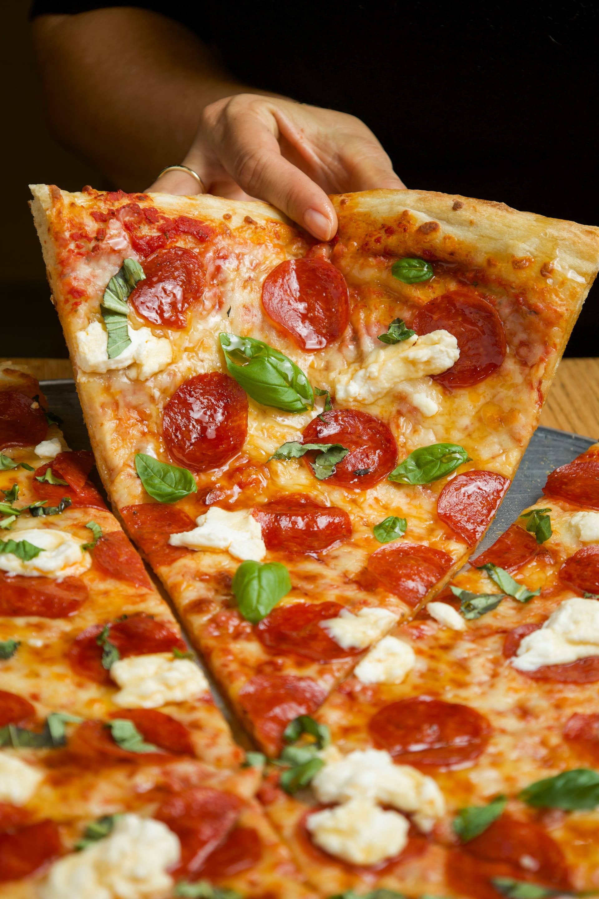 Porción de pizza de pepperoni con burrata, levantada de la bandeja.