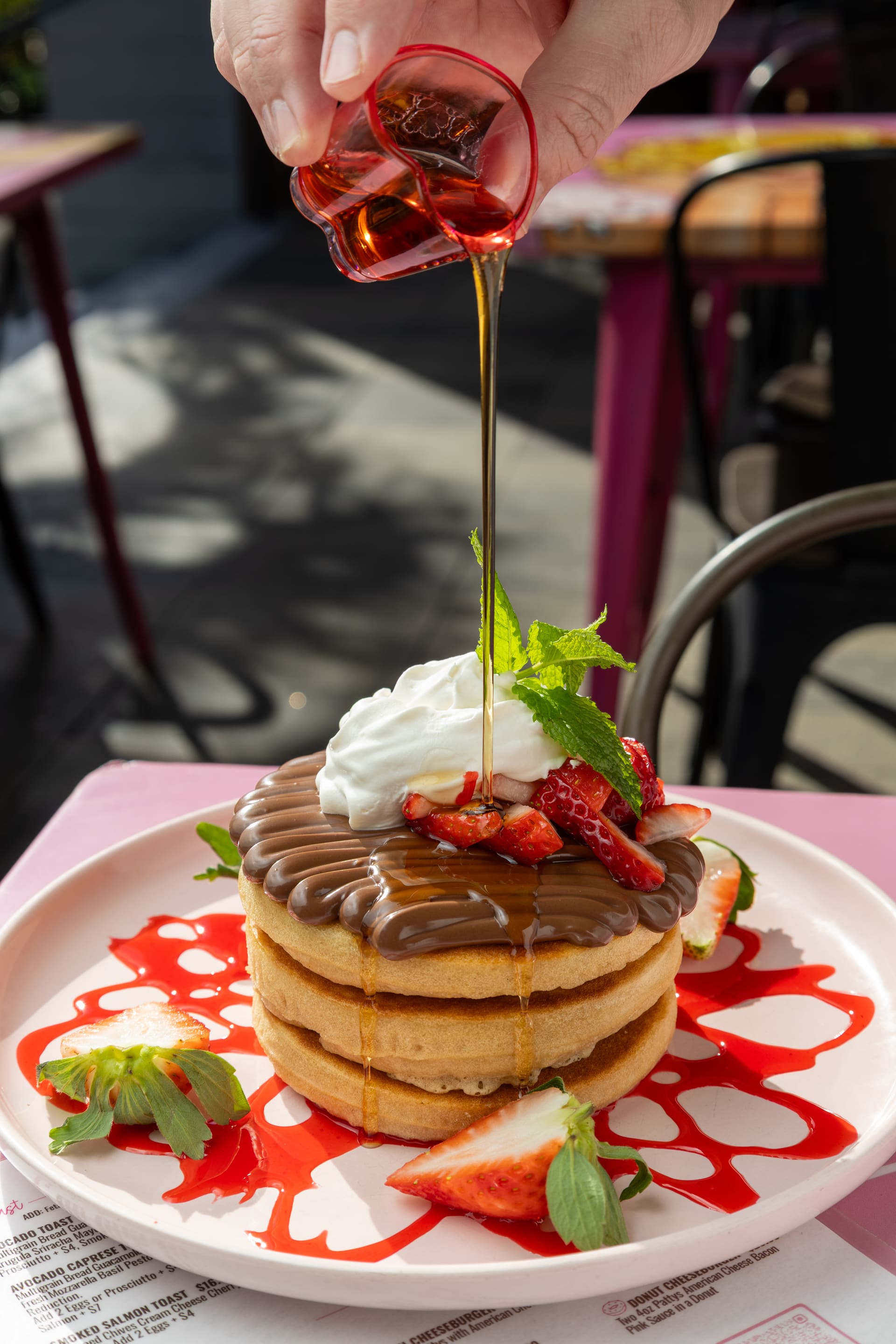 Sirope cayendo sobre una torre de pancakes con frutillas.