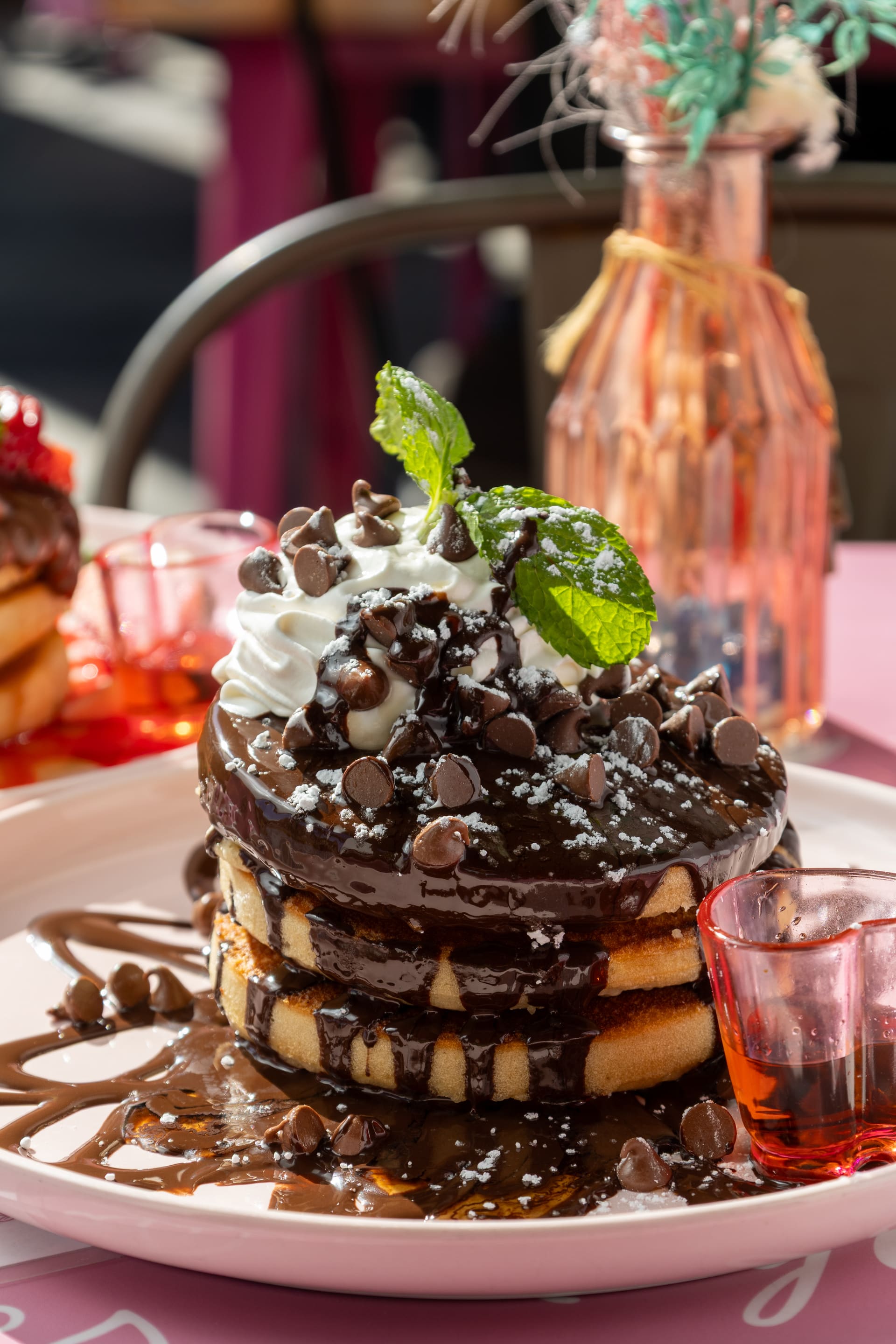 Pancakes de chocolate con crema y menta sobre plato rosa.