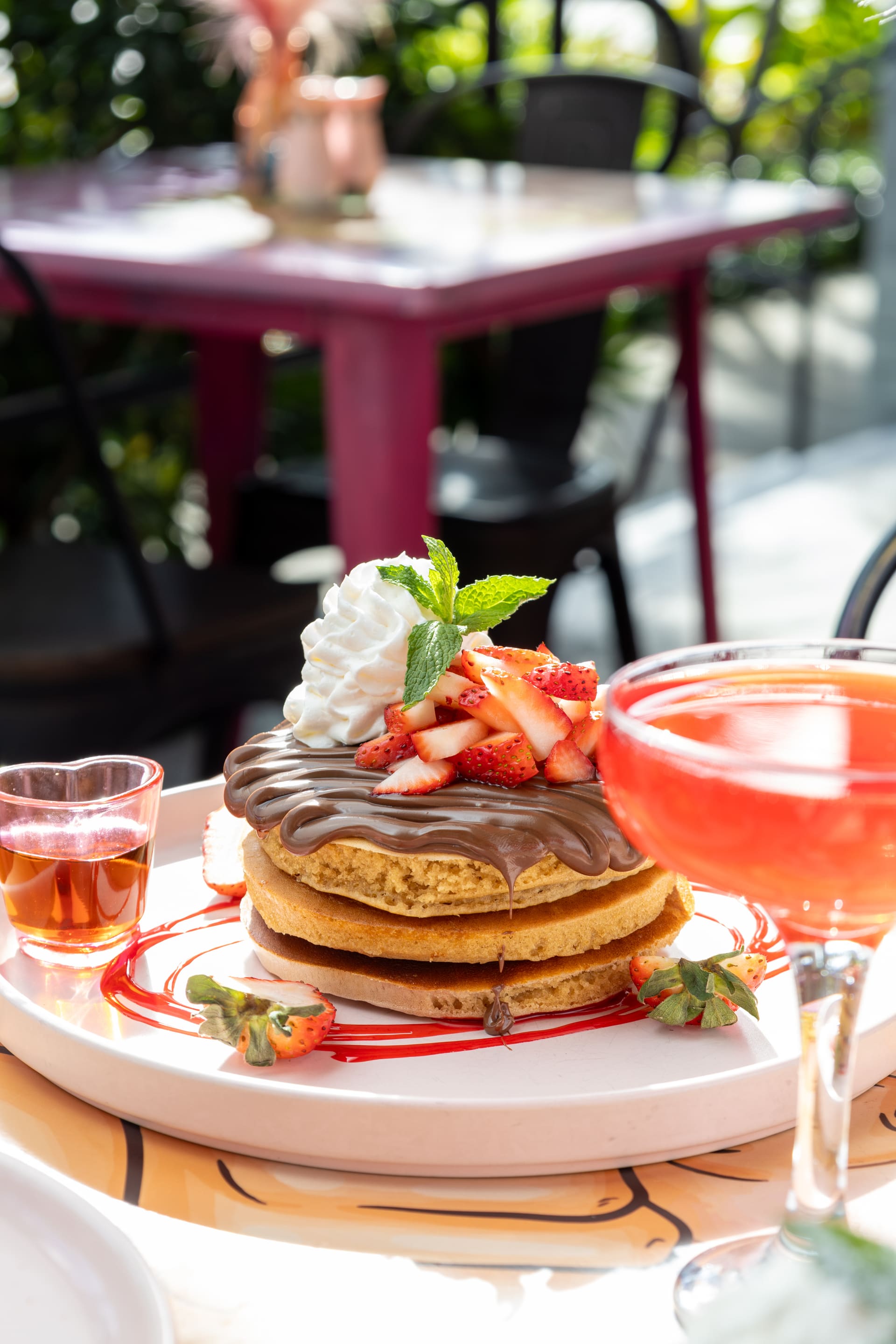 Mesa con pancakes y un cóctel rosado en terraza.