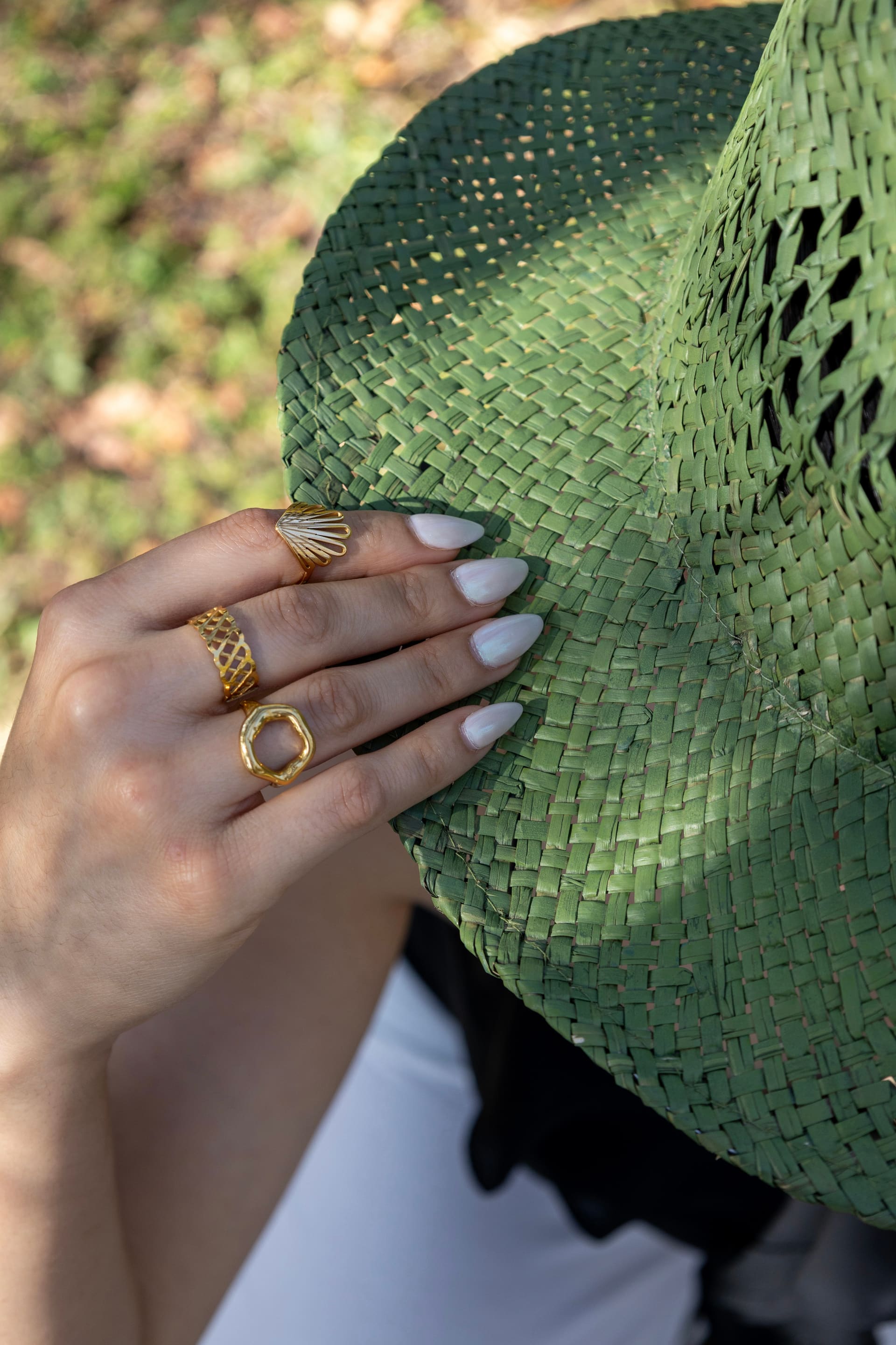 Mano con anillos dorados sosteniendo un sombrero de paja verde.